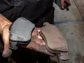 Mani sporche di grasso tengono due pastiglie freni: una nuova e una consumata.