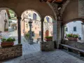 Un vicolo tra i borghi della montagna pistoiese, con archi in pietra, colonne e vasi di fiori rossi.