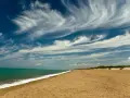 Spiaggia dorata e mare turchese al parco costiero di Rimigliano, con un cielo blu intenso solcato da nuvole bianche e leggere.
