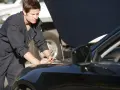 Meccanico in tuta blu lavora sul motore di un'auto nera. La revisione auto si può fare in tutta Italia, ovunque ci sia un professionista.