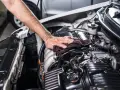 Mano che pulisce il motore dell'auto con un panno. Non è consigliabile usare l'idropulitrice per lavare il motore della macchina.