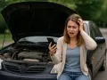 Ragazza disperata guarda il telefono, cofano aperto, la macchina non parte cause sconosciute.