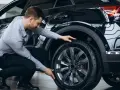 Uomo in ginocchio effettua il controllo gomme auto, esaminando il battistrada del pneumatico nero.
