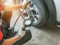 Controllo pressione gomme a caldo o freddo con manometro. Un meccanico in tuta rossa verifica la pressione degli pneumatici.