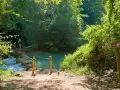 Sentiero naturalistico con guado su fiume, ideale per percorsi trekking Toscana. Segnale Via Francigena indica la direzione.