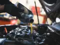 Mano con guanto versa olio motore. Il cambio olio ogni quanto è fondamentale per la salute dell'auto.