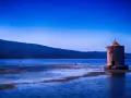 Mulino solitario in un'oasi WWF Toscana, con acque blu e colline sullo sfondo.