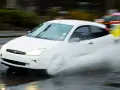 Auto bianca in movimento su strada bagnata, creando un'onda d'acqua a causa del fenomeno aquaplaning.