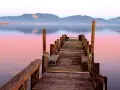 Pontile in legno su lago calmo al tramonto, con montagne sullo sfondo. Si intuisce dove si trova Torre del Lago.