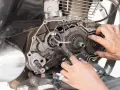 Mani che lavorano sul motore di una moto, forse per risolvere una perdita di potenza auto benzina. Ingranaggi e parti meccaniche in vista.
