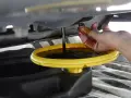 Cambio olio: un tappo sporco di olio viene tenuto da una mano mentre l'olio esausto cola in un contenitore. Forse c'era troppo olio nel motore.