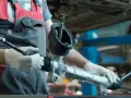 Meccanico con guanti tiene una scatola dello sterzo rotta. Sintomi di guasto includono rumori e difficoltà di sterzata.