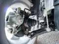Parti della sospensione di un'auto, inclusa la pinza del freno e il giunto omocinetico con soffietto, utili per riconoscere i sintomi di un semiasse auto rotto.