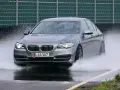 BMW grigia in test di acquaplaning, solleva un'onda d'acqua mentre sfreccia sull'asfalto bagnato.