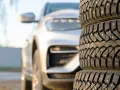 Gomme invernali con chiodi in primo piano, un'auto bianca sfocata sullo sfondo. Preparazione per l'inverno, anche se è estate.