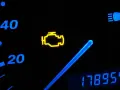 Cruscotto auto con spia motore accesa. La spia gialla a forma di motore indica un problema. Oltre, indicatori di velocità e chilometraggio.