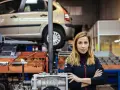Donna in officina con auto sollevata, pronta per la manutenzione straordinaria auto.