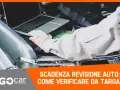 Meccanico con guanti controlla la scadenza della revisione auto tramite laptop, con il cofano aperto.