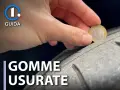 Una mano controlla l'usura di un pneumatico con una moneta da 1 euro. La tela del pneumatico è visibile, mostrando quanto sia consumata.