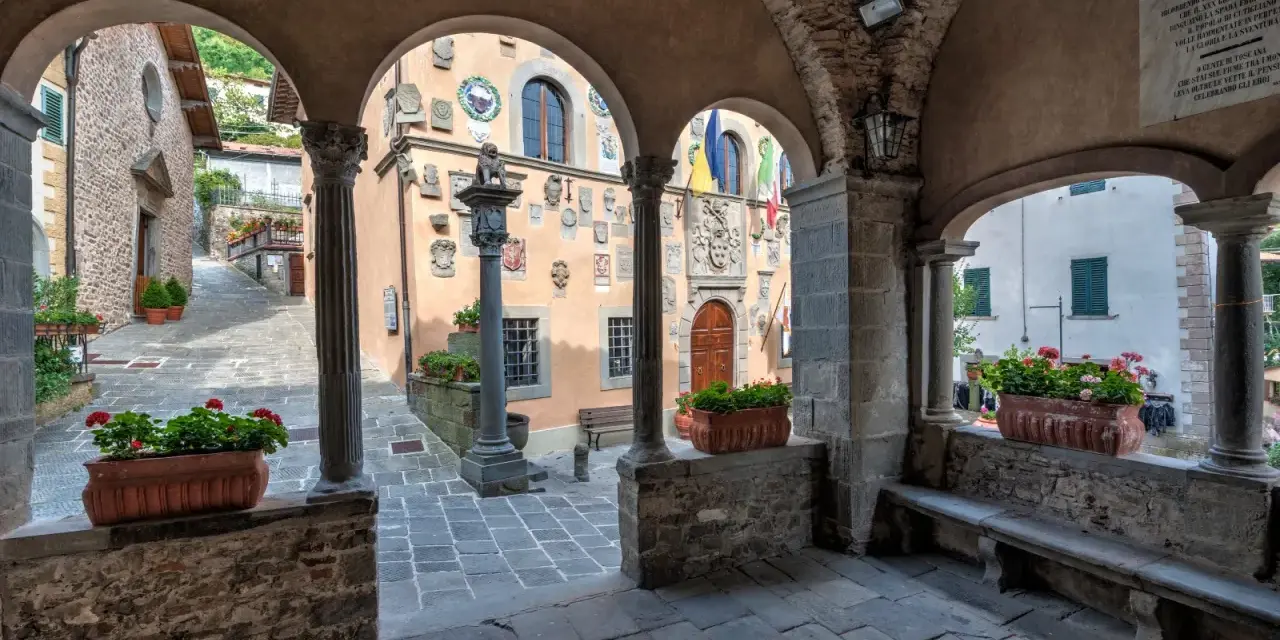Un vicolo tra i borghi della montagna pistoiese, con archi in pietra, colonne e vasi di fiori rossi.