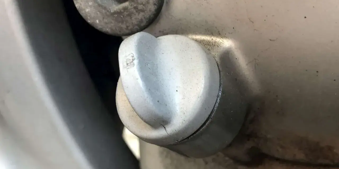 Dettaglio di un tappo motore con una piccola crepa, suggerendo una possibile fuoriuscita olio motore dal tappo.