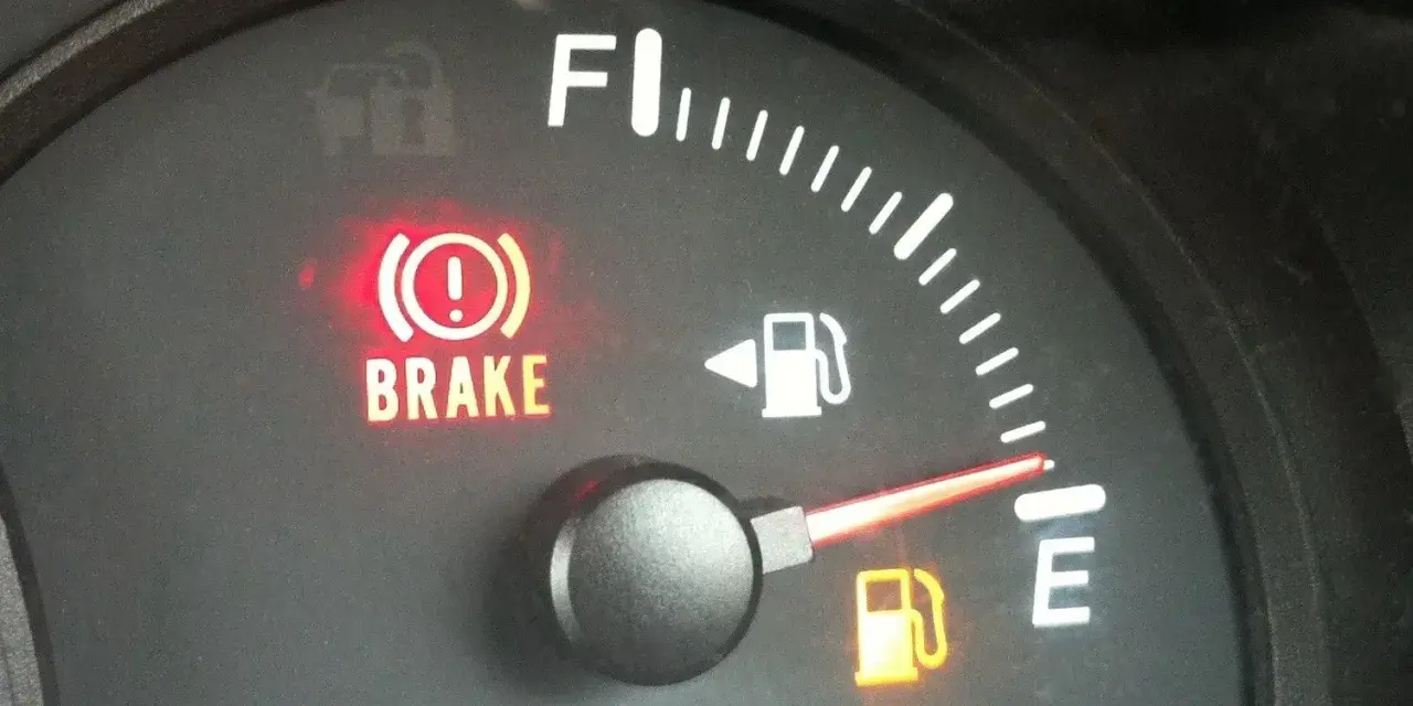 Cruscotto auto con spia freno a mano accesa e indicatore carburante quasi vuoto. È ora di fare rifornimento e resettare l'indicatore carburante.