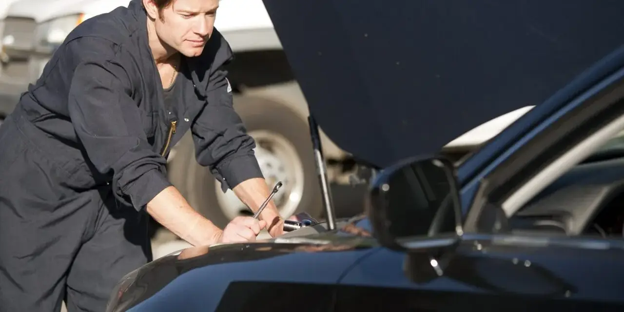 Meccanico in tuta blu lavora sul motore di un'auto nera. La revisione auto si può fare in tutta Italia, ovunque ci sia un professionista.