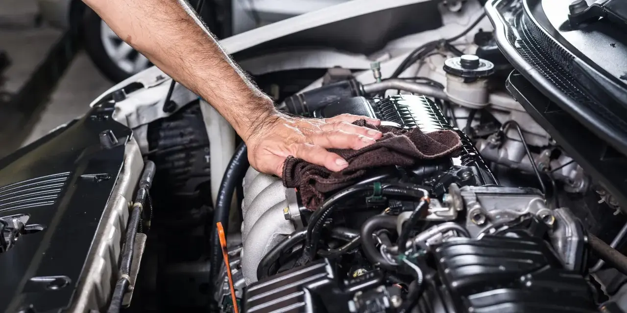 Mano che pulisce il motore dell'auto con un panno. Non è consigliabile usare l'idropulitrice per lavare il motore della macchina.