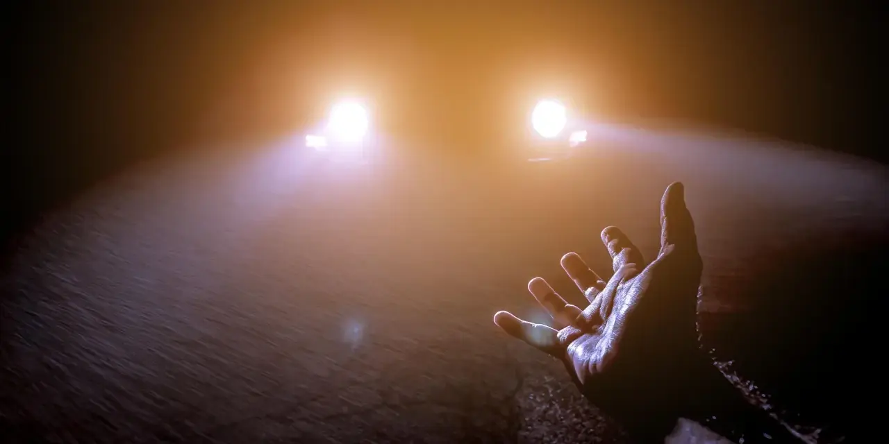 Mano tesa verso le luci abbaglianti di un'auto nella nebbia, un momento di incertezza e speranza.