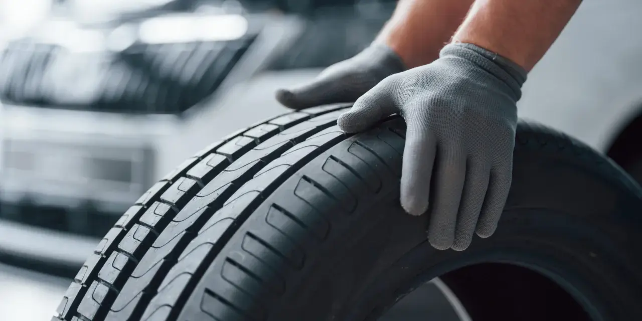 Mani guantate controllano il battistrada di uno pneumatico, valutando la sua durata gomme auto.