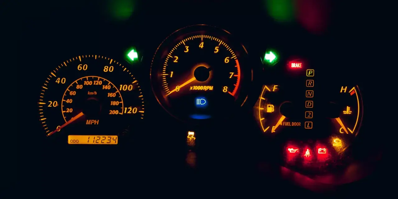 Cruscotto auto illuminato di arancione: tachimetro, contagiri, indicatori di marcia e spie accese, tra cui una spia arancione macchina.