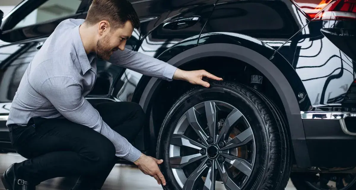Uomo in ginocchio effettua il controllo gomme auto, esaminando il battistrada del pneumatico nero.
