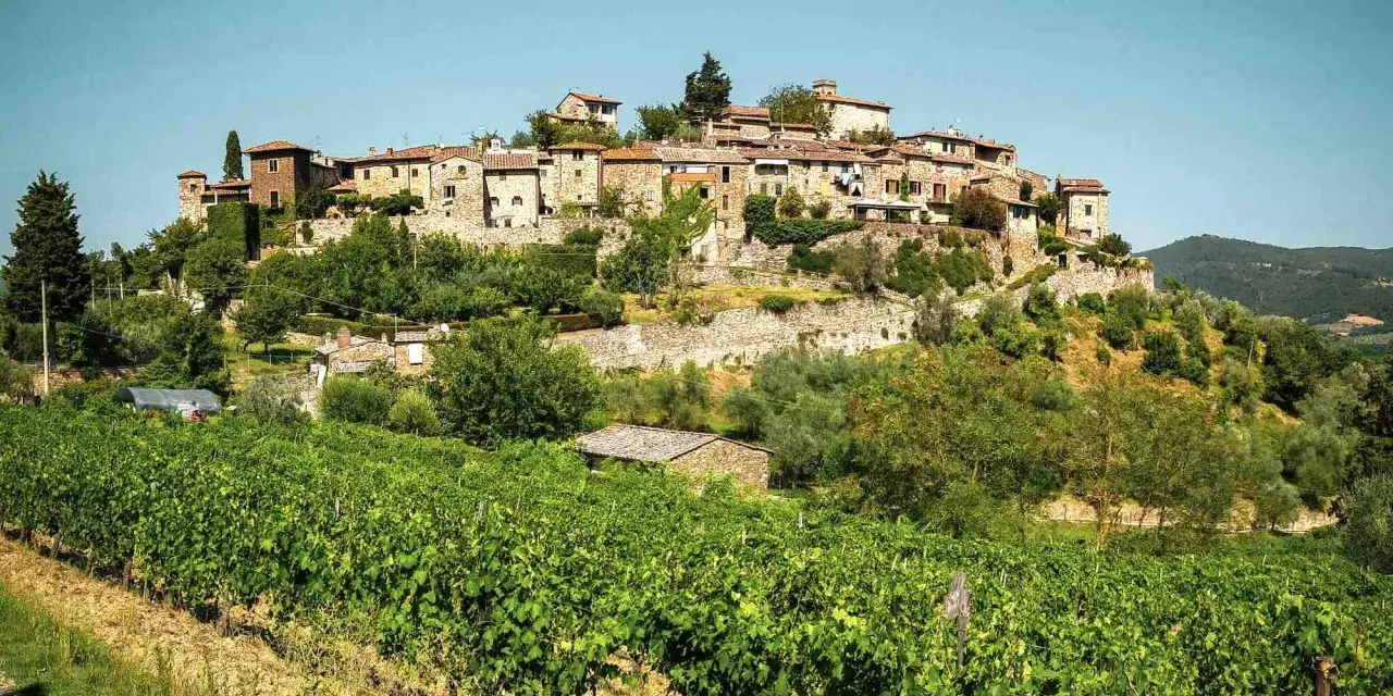 Borgo medievale su una collina, circondato da vigneti e ulivi. Le bandiere arancioni toscana sventolano tra le case di pietra.