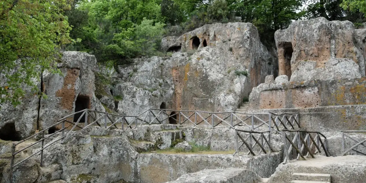 Antiche tombe scavate nella roccia, parte dei siti etruschi in Toscana, con sentieri e recinzioni in legno.