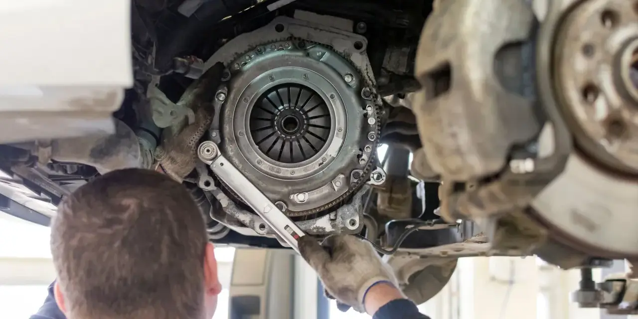 Meccanico lavora sulla frizione di un'auto. La durata della frizione varia, ma si consiglia di controllarla ogni quanti km si cambia la frizione.