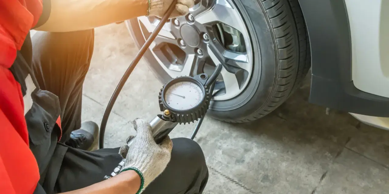 Controllo pressione gomme a caldo o freddo con manometro. Un meccanico in tuta rossa verifica la pressione degli pneumatici.