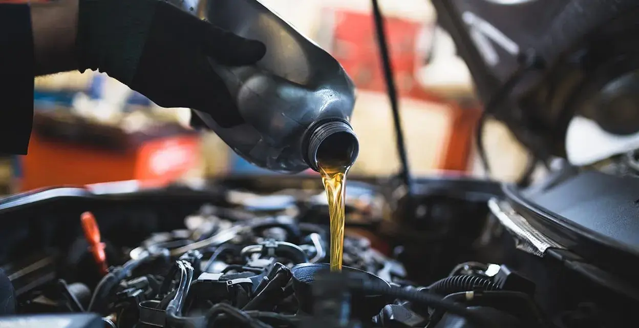 Mano con guanto versa olio motore. Il cambio olio ogni quanto è fondamentale per la salute dell'auto.