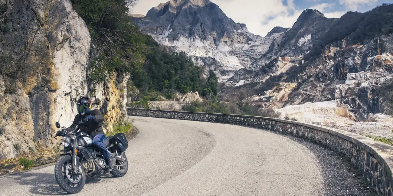 Un motociclista percorre una strada tortuosa tra le cave di marmo delle Alpi Apuane, un'avventura tra i passi toscana moto.