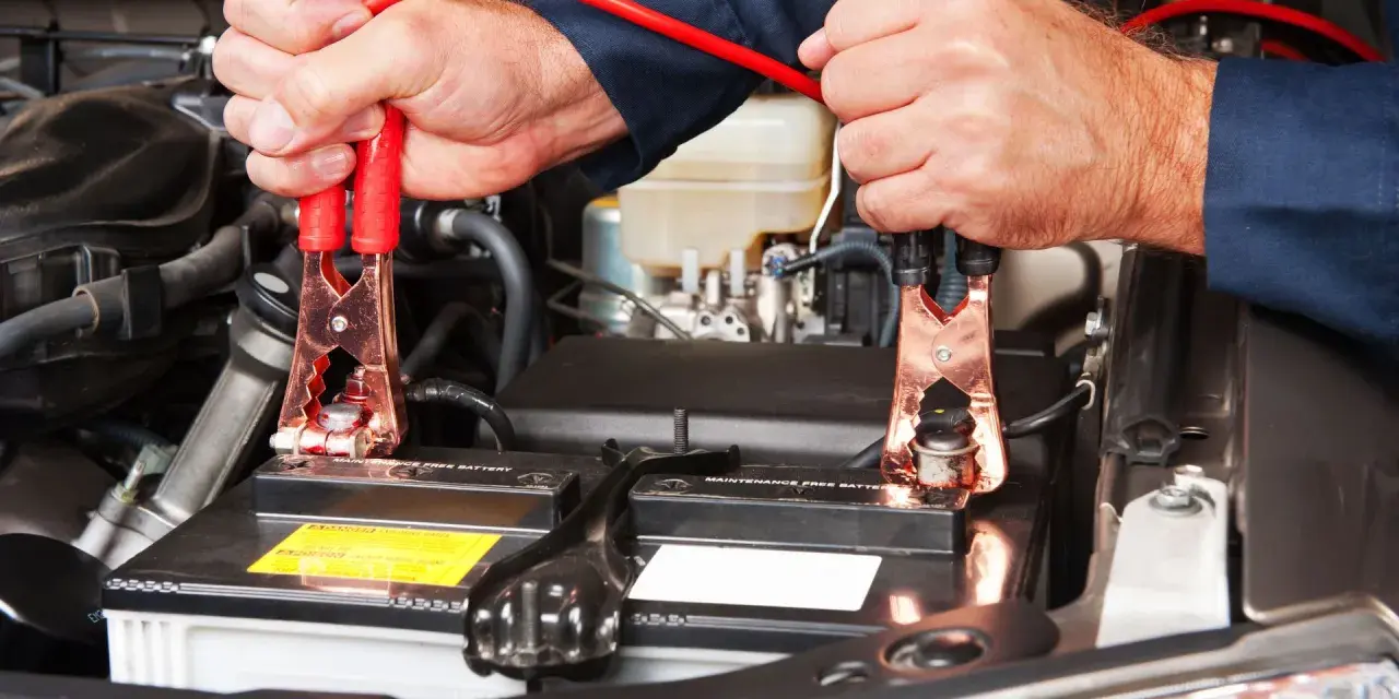 Mani che collegano i cavi alla batteria per capire come far ripartire la macchina.