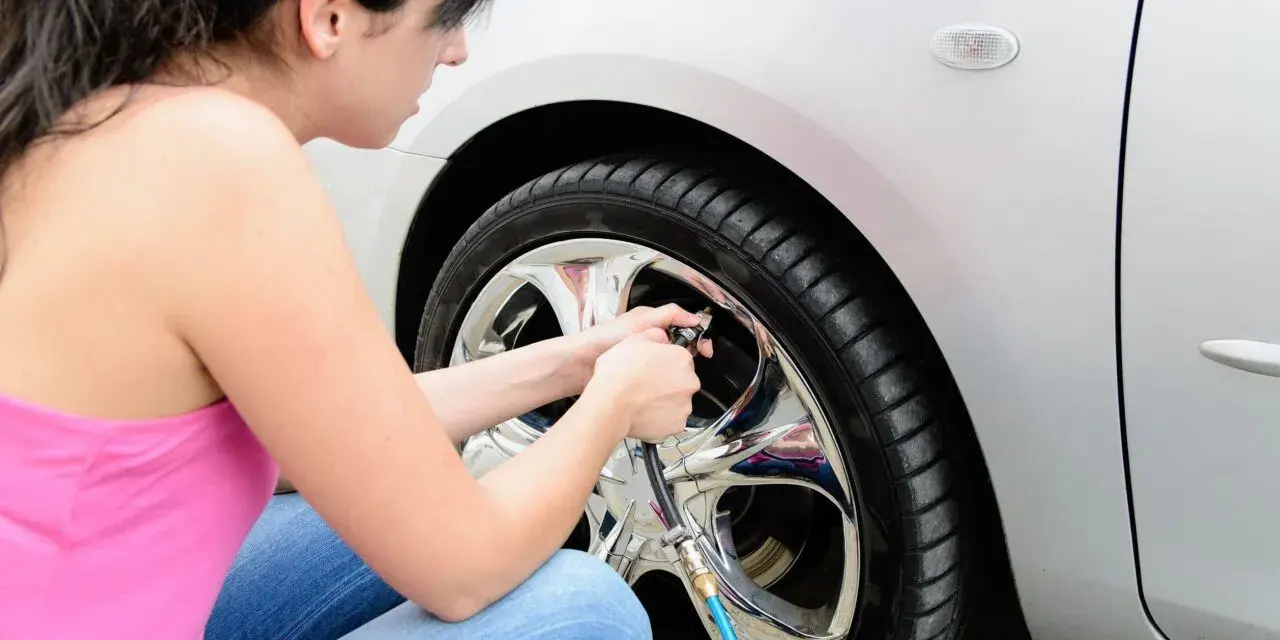 Donna controlla la pressione gomme auto estate, assicurandosi che siano gonfie al punto giusto per un viaggio sicuro.