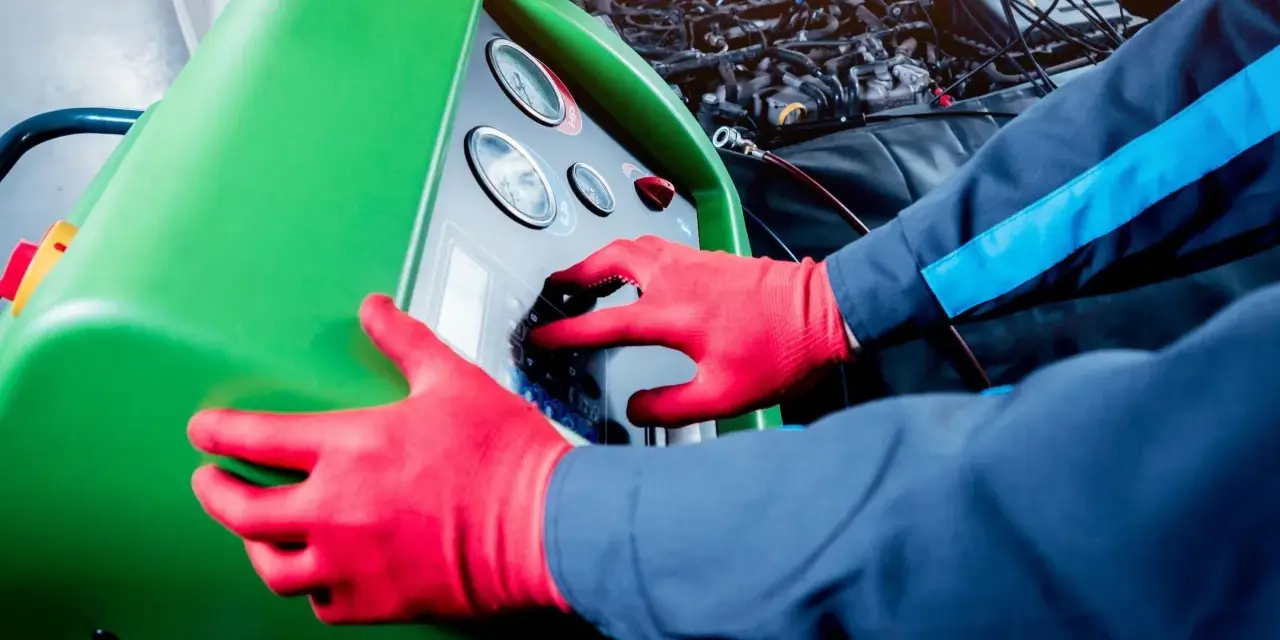 Tecnico con guanti rossi usa una macchina per controllare la perdita gas condizionatore auto.