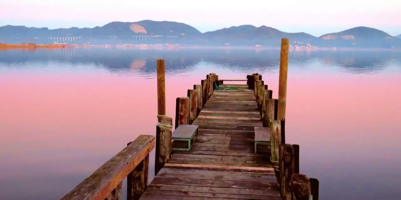 Pontile in legno su lago calmo al tramonto, con montagne sullo sfondo. Si intuisce dove si trova Torre del Lago.