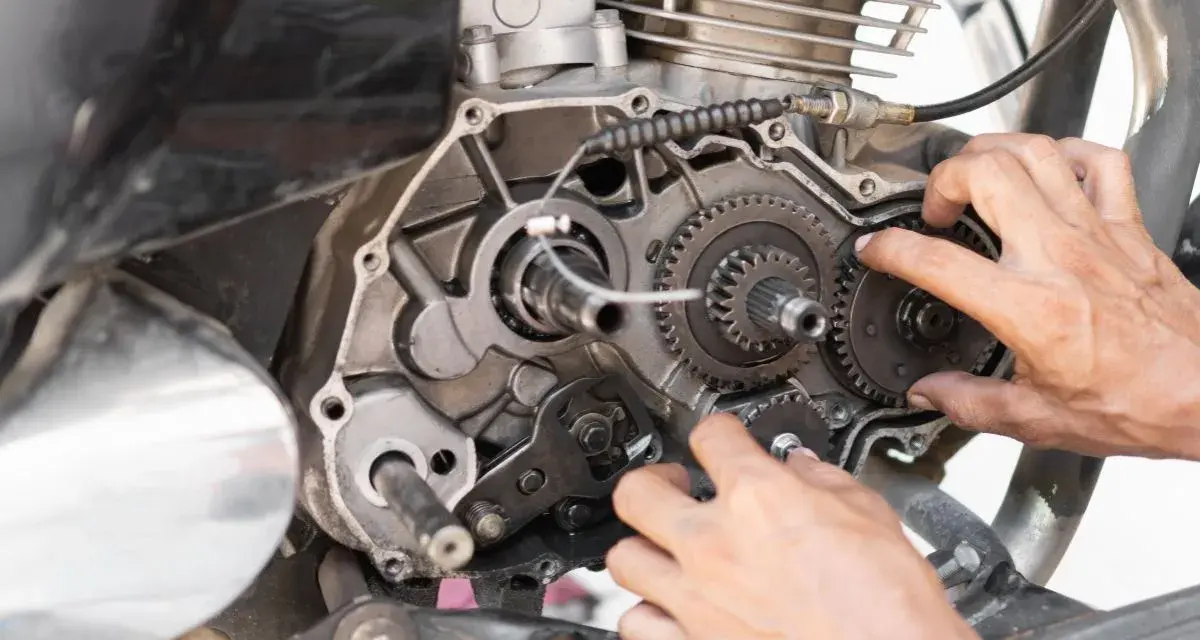 Mani che lavorano sul motore di una moto, forse per risolvere una perdita di potenza auto benzina. Ingranaggi e parti meccaniche in vista.