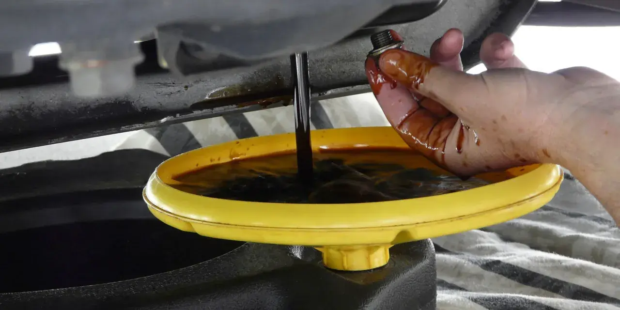 Cambio olio: un tappo sporco di olio viene tenuto da una mano mentre l'olio esausto cola in un contenitore. Forse c'era troppo olio nel motore.