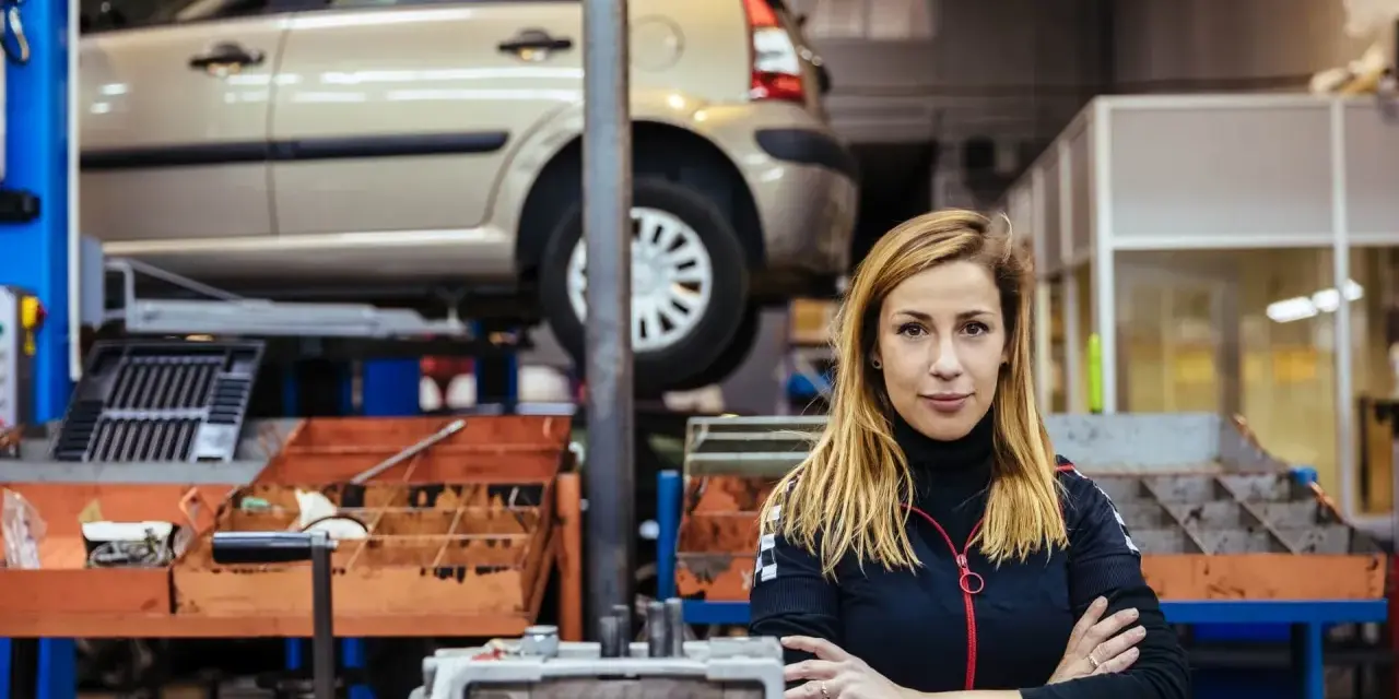 Donna in officina con auto sollevata, pronta per la manutenzione straordinaria auto.