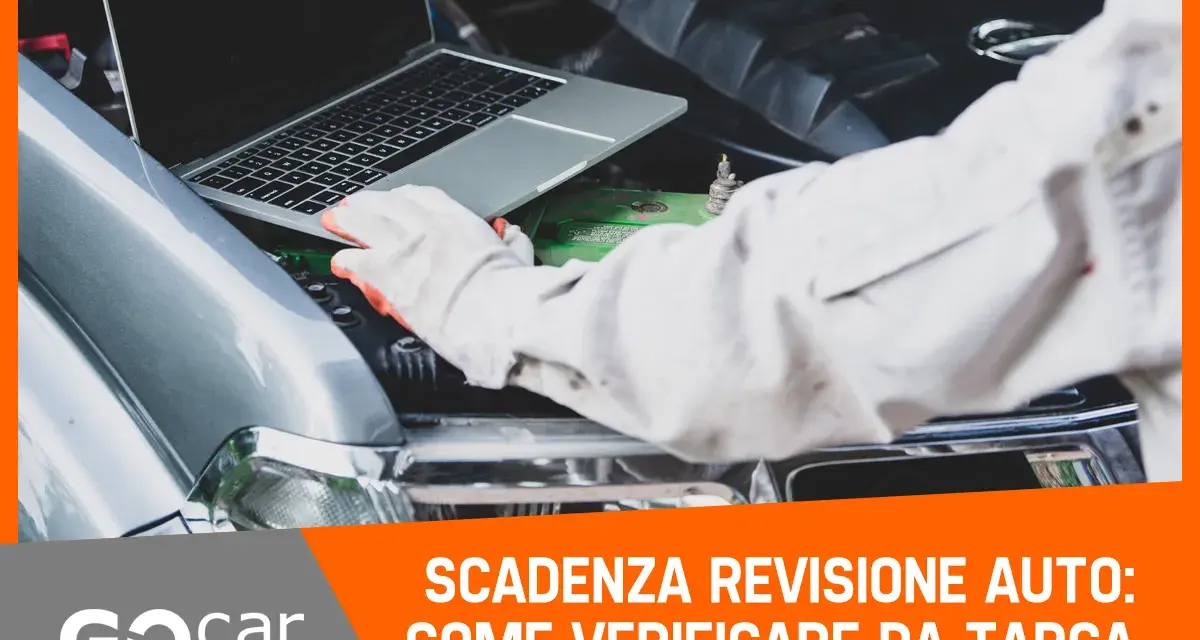 Meccanico con guanti controlla la scadenza della revisione auto tramite laptop, con il cofano aperto.