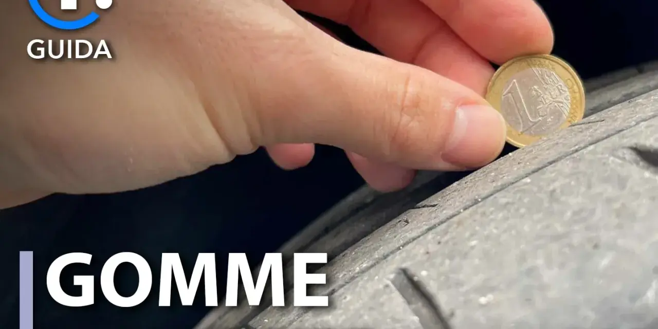 Una mano controlla l'usura di un pneumatico con una moneta da 1 euro. La tela del pneumatico è visibile, mostrando quanto sia consumata.