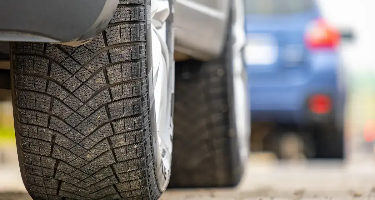 Primo piano di pneumatici invernali, con un'altra auto in lontananza. La classe rumorosità pneumatici è un fattore importante per il comfort di guida.