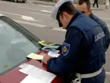 Agente di polizia scrive verbale su un'auto con revisione scaduta da 2 anni. Documenti e patente sul cofano.
