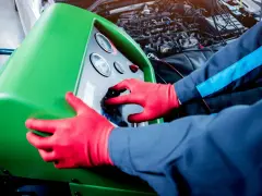 Tecnico con guanti rossi usa una macchina per controllare la perdita gas condizionatore auto.